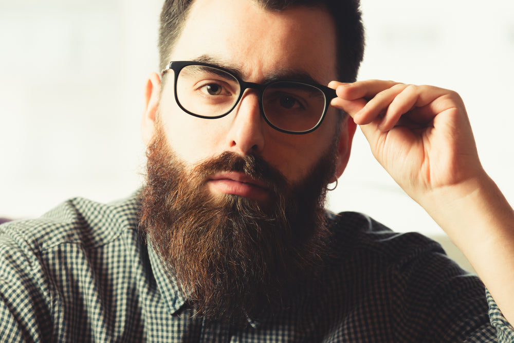 man looks at the camera as he adjusts his glasses