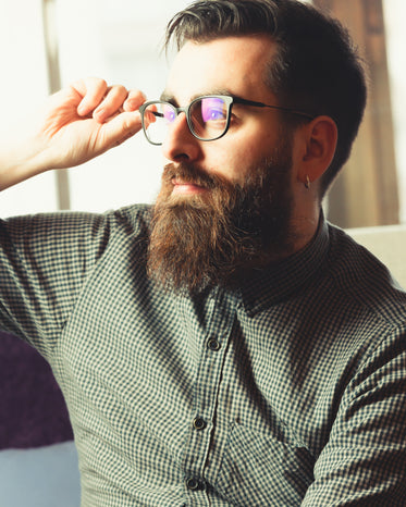 man looks to the left as he adjusts his glasses