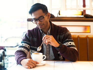 man pulls spoon from coffee at cafe after a stir