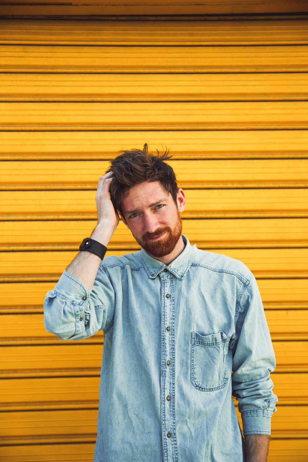 man scratches head in front of yellow door