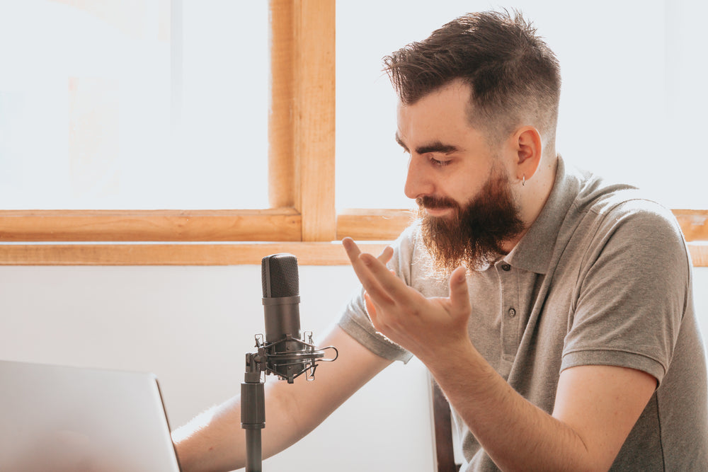 man sits in front of a black microphone and his laptop