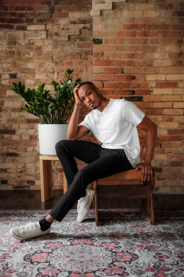 man sits in front of a red brick wall and poses