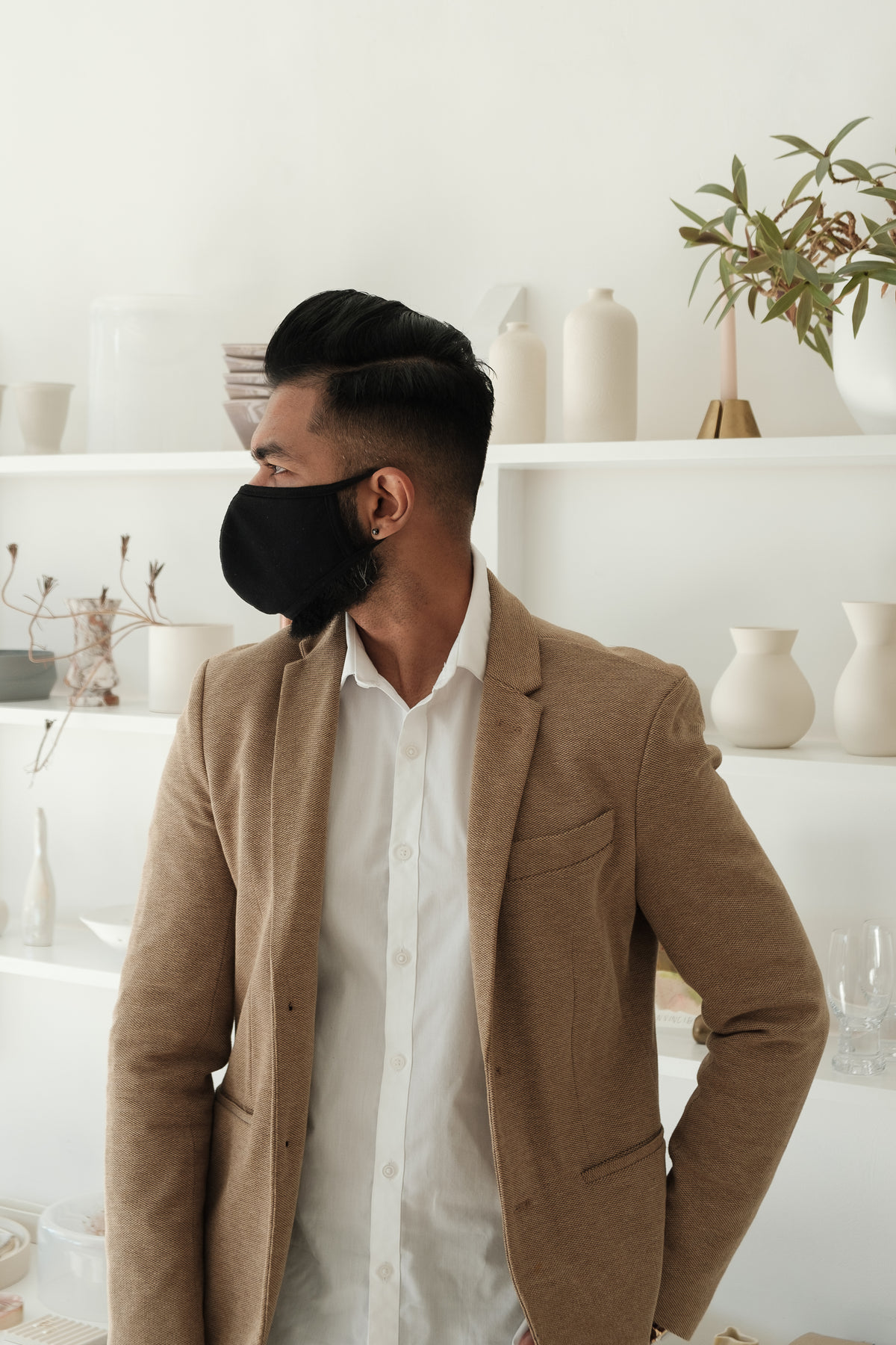 homem em frente a uma estante com objetos usando máscara facial preta