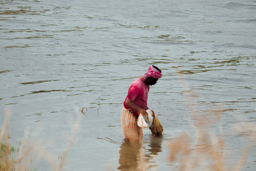 man wading through water with fishing net in india