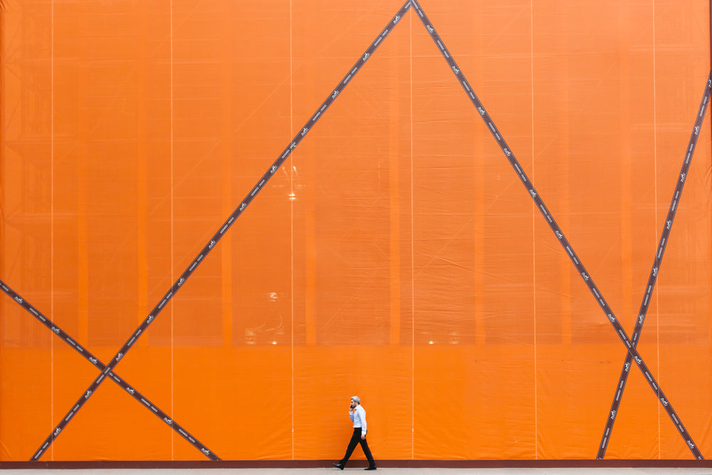 homem caminhando e parede laranja