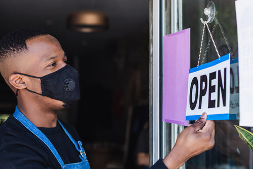 man wearing face mask flips open sign