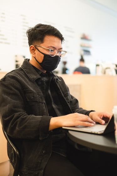 man works on his laptop and wears facemask