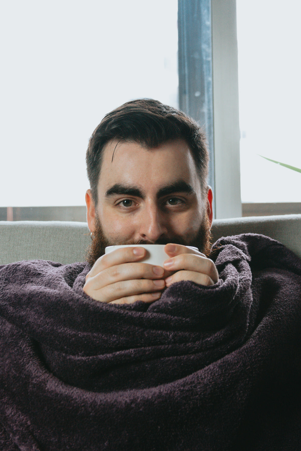 man wrapped in blanket and holding bowl close to his face
