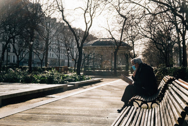 masked person reads a newspaper in the park