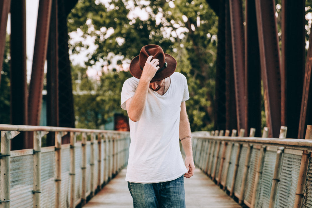 men's fashion walking across bridge holding hat