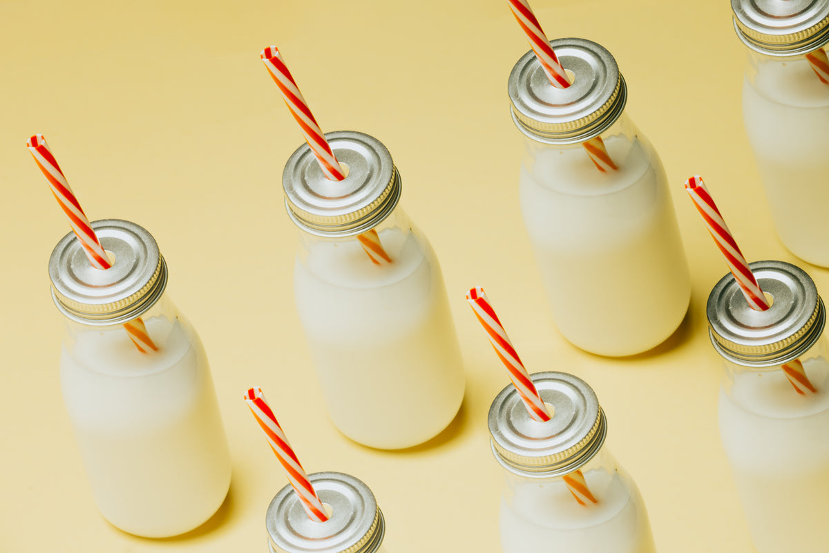 milk bottles with red striped straws on a yellow surface