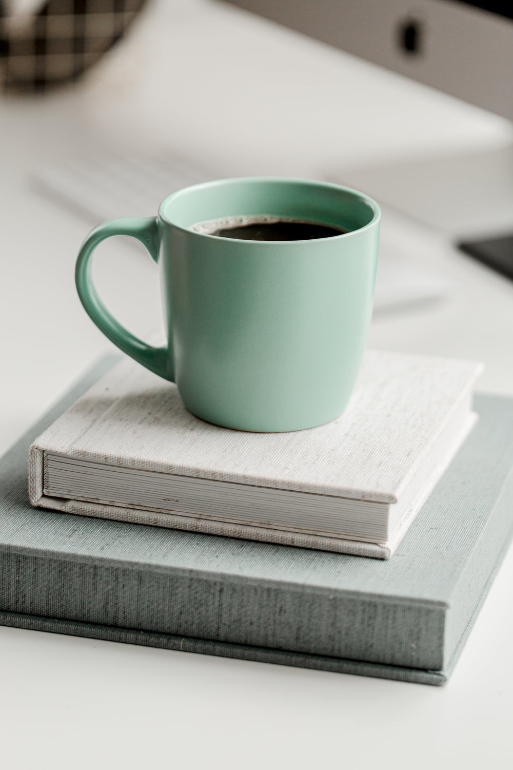 mint green mug full of black coffee on top of books