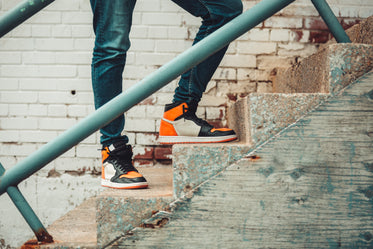model in black and orange sneakers perched atop stairs