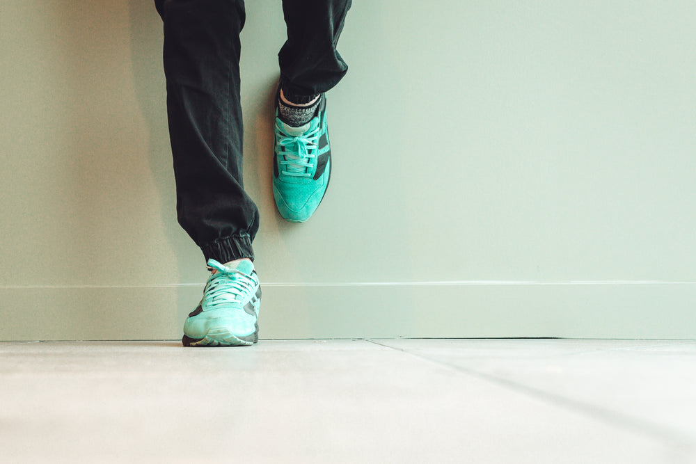 model in green sneakers and black denim leaning on wall