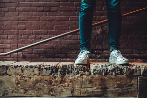 model in speckled sneakers standing atop rustic wood ledge