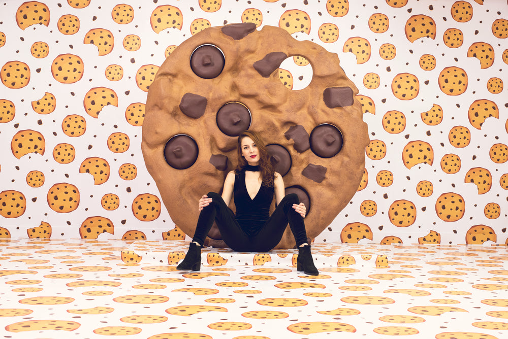 model sits in front of a giant cookie in a cookie-themed room