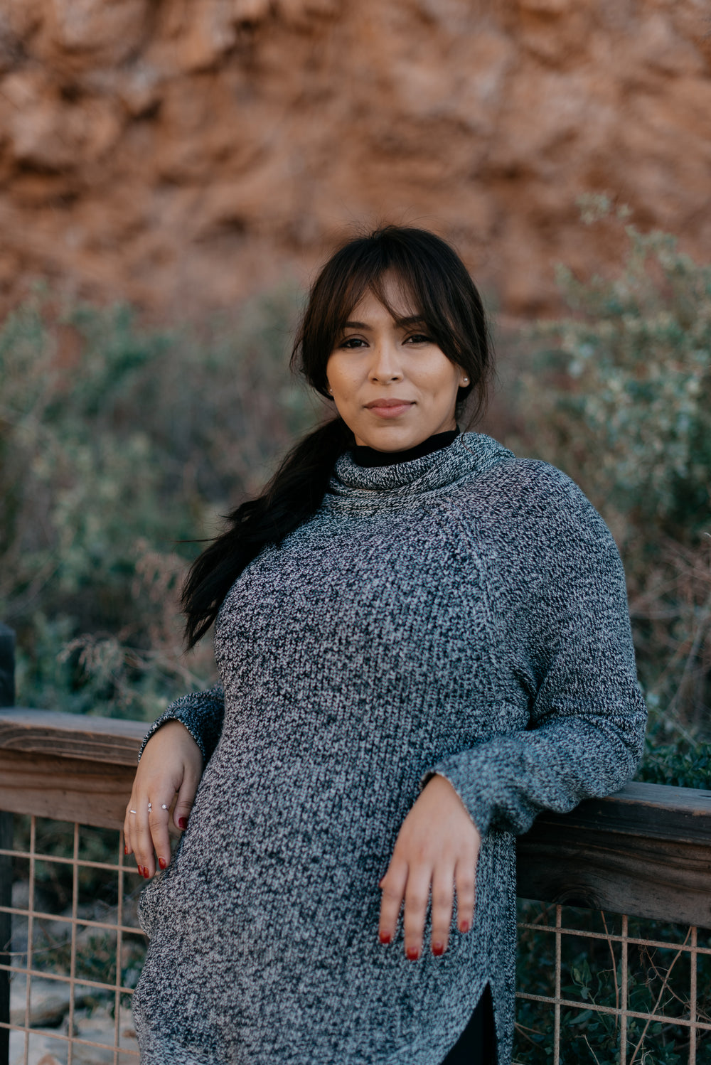 model wearing a wooly sweater leans against a railing