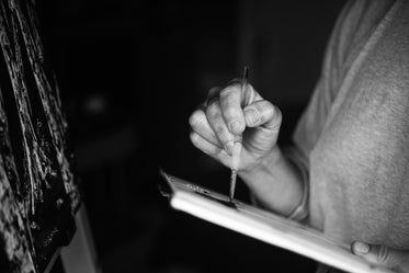 monochrome hand holding a paint brush to a pallet