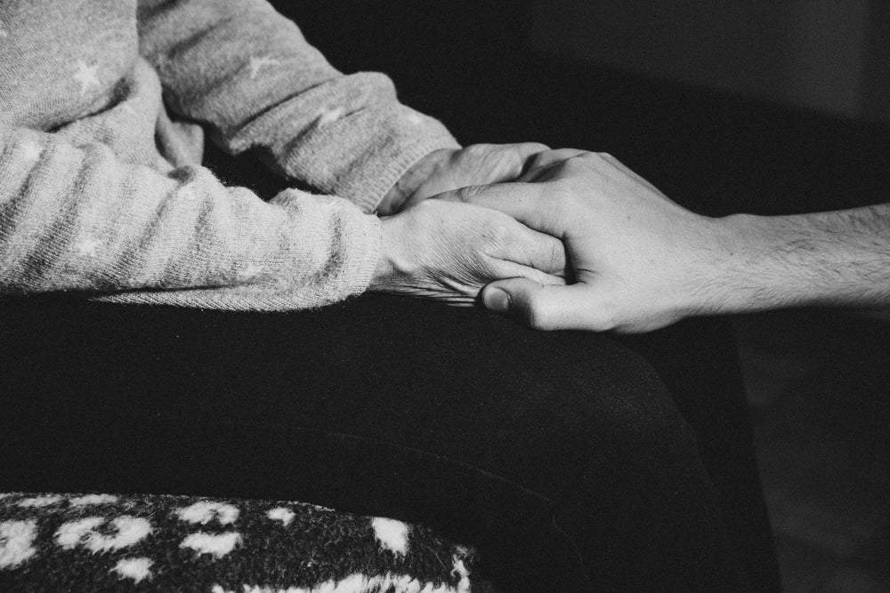 monochrome image of person holding someones elses hand