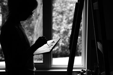 monochrome photo of a person painting on an easel