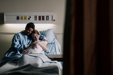 mother and father embrace in hospital bed while admiring baby