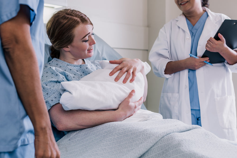 mother smiles as she holds newborn baby while resting in bed