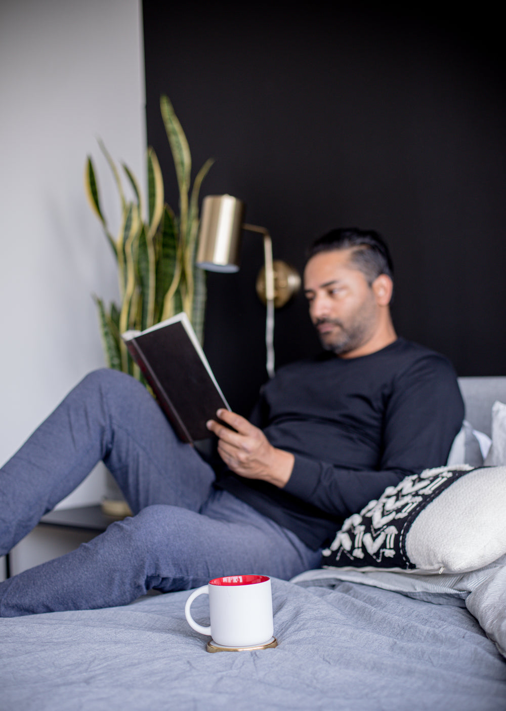 mug on a grey bed with a person reading out of focus