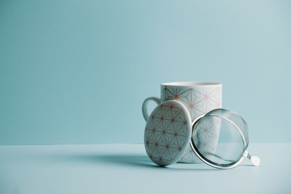 mug with a lid and strainer sits against a blue background