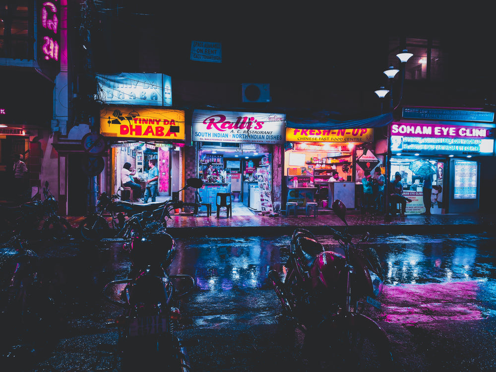 neon shop lights reflect on rain-wet streets in india