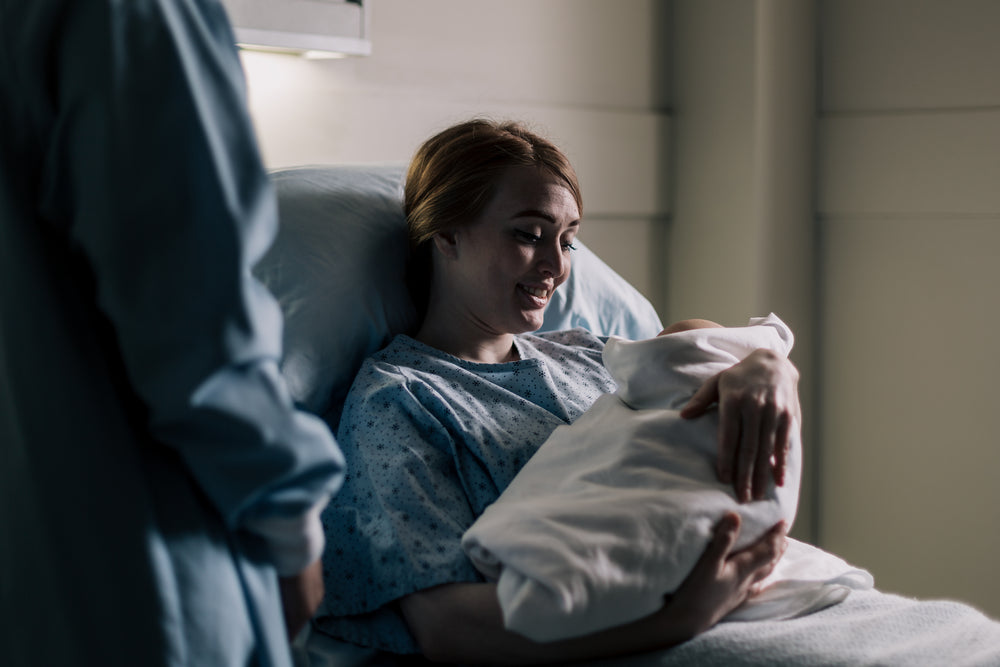 new mother smiling at her baby while resting in hospital bed