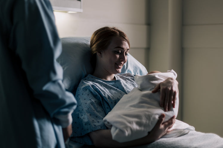 New Mother Smiling At Her Baby While Resting In Hospital Bed