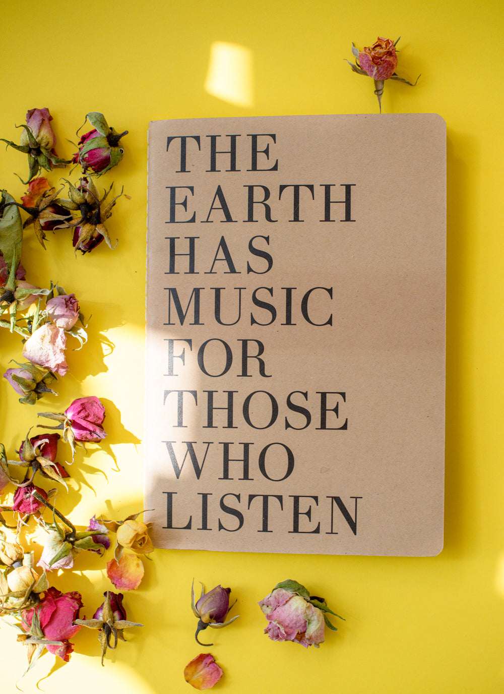 notebooks lays on a yellow surface with dried flowers surrounding