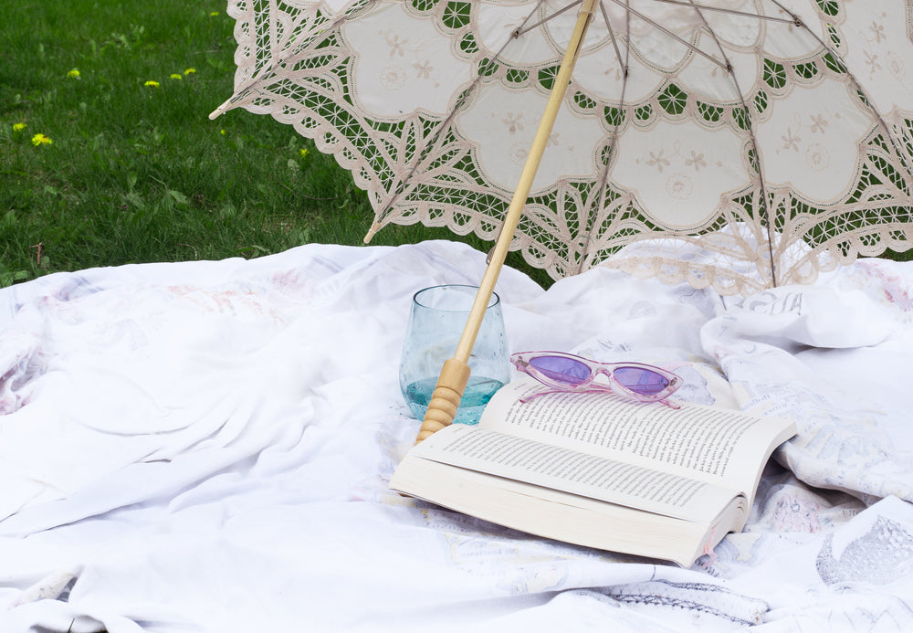 novel lays open under a cloth parasol on a picnic blanket