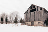 old barn with missing section surrounded by snow