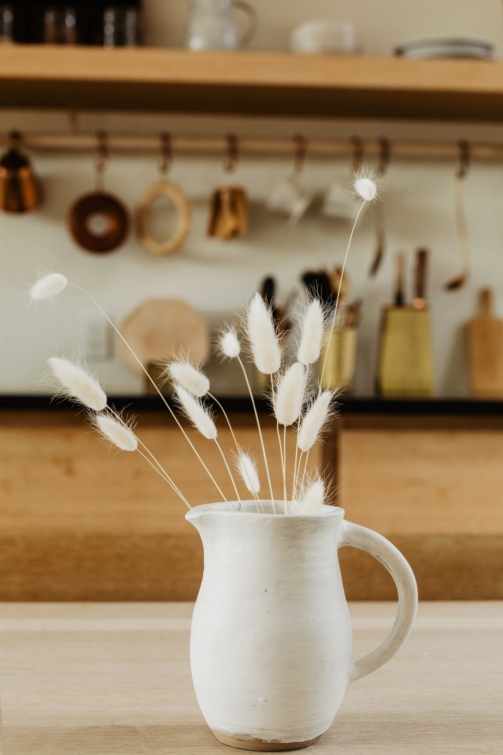 old white dandelions in a white jug on a wooden table