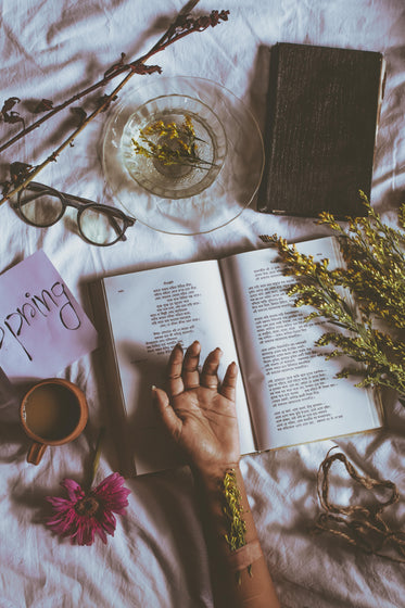 open novel with a hand on it by dried flowers