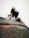 paint brushes burst from a glittery handbag