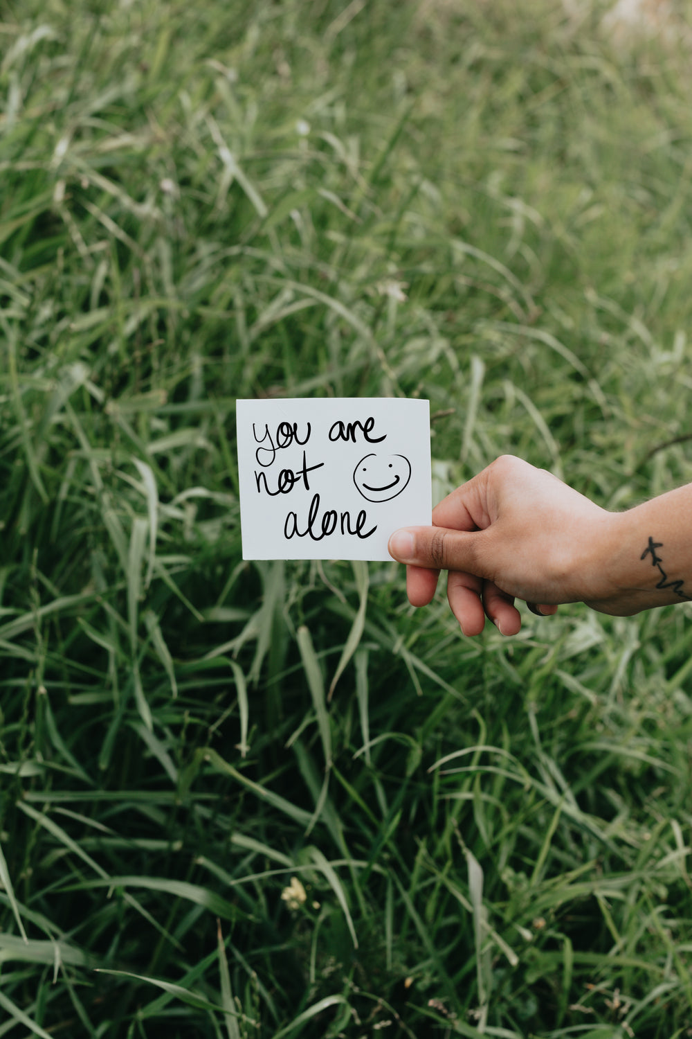 paper reads you are not alone against tall grass