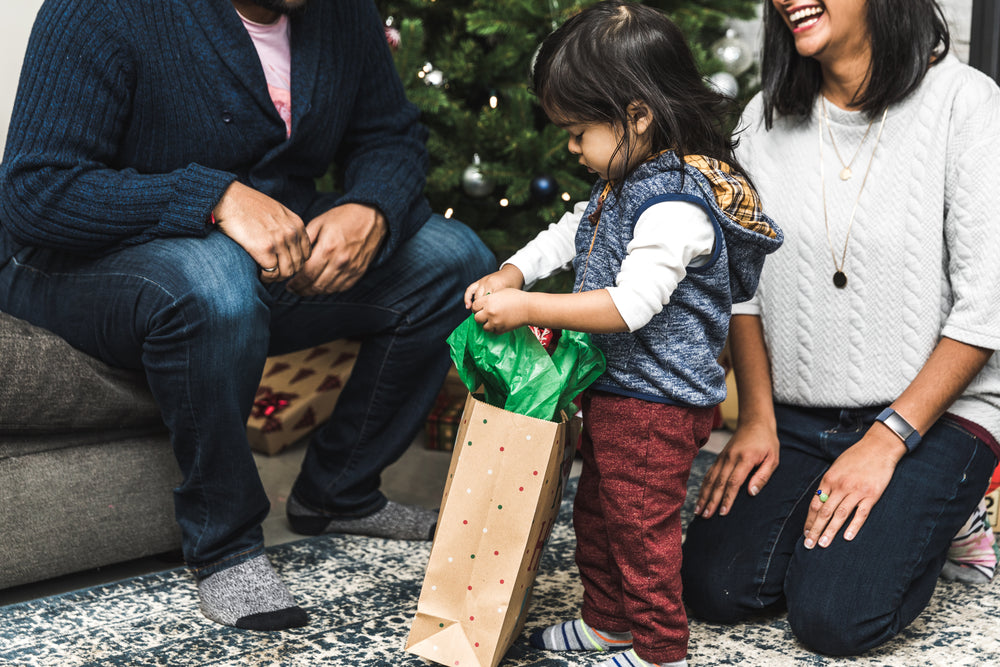 pais observam o filho abrir os presentes de natal