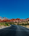 paved road bends with red rocky hills in the background
