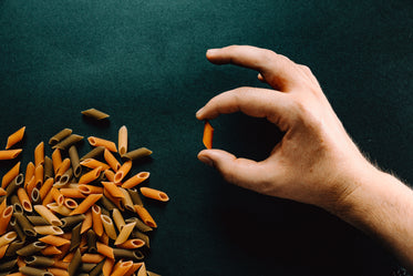 penne pasta shells and a hand against a black background