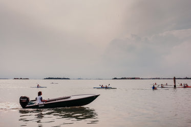 people kayak on a cloudy day with a boat following