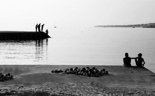 people silhouetted looking at the water in black and white