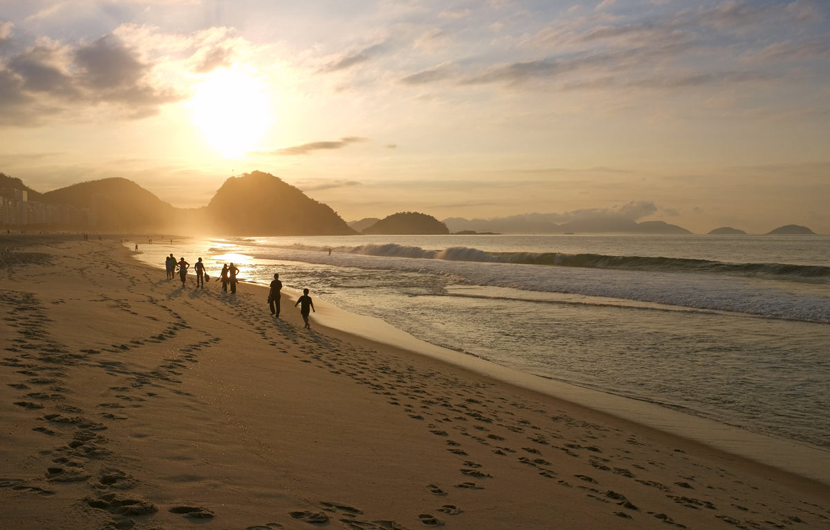 people walking down a sandy beach at sunset