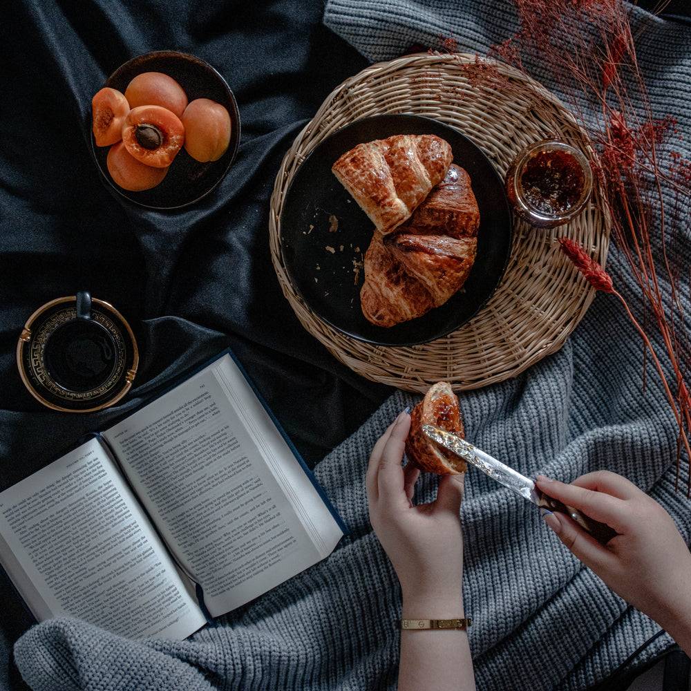 person adding jam to a croissant with a butter knife