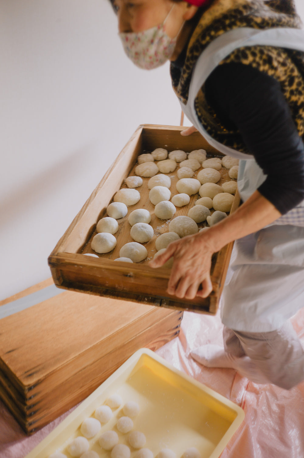 person carries a wooden box full of dough balls