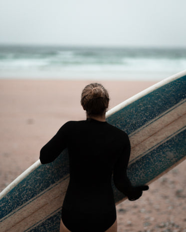 person carries their blue and white surfboard to the ocean