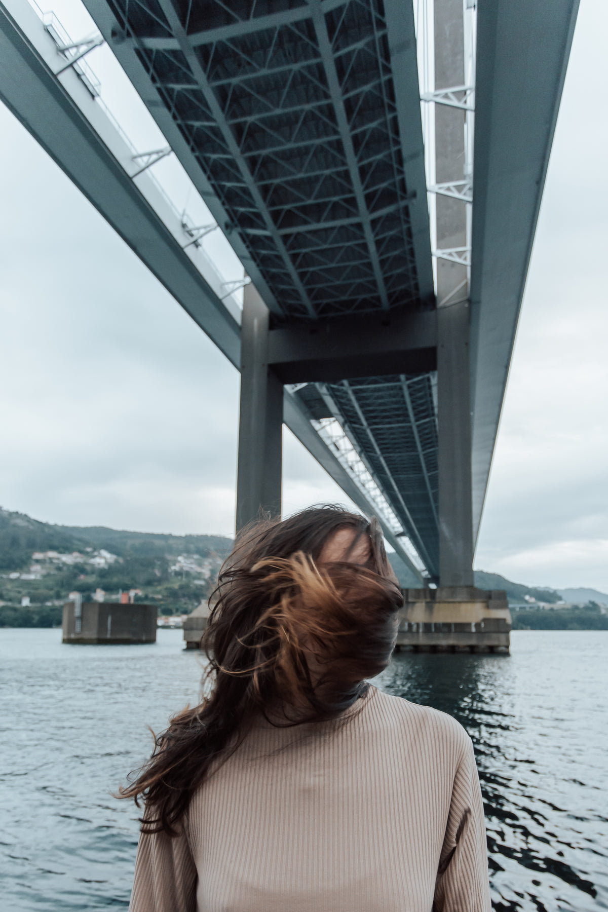 person covered by hair stands under bridge on a windy day
