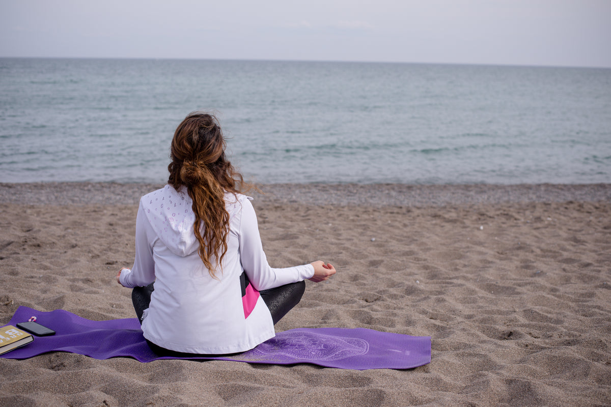 person cross legged on a yoga mat at the beach