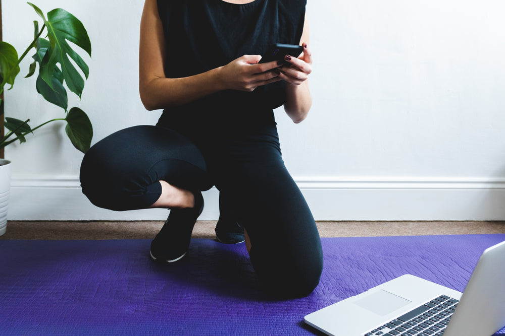 person crouches on purple yoga mat looking at their phone